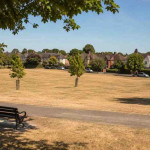Brown summer grass in a residential park surrounded by Irish homes during the July heatwave, illustrating the importance of seasonal property maintenance.